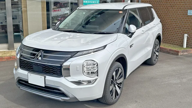 Mitsubishi Outlander PHEV de la generación actual, blanco, aparcado ante un concesionario, visto de tres cuartos delantero